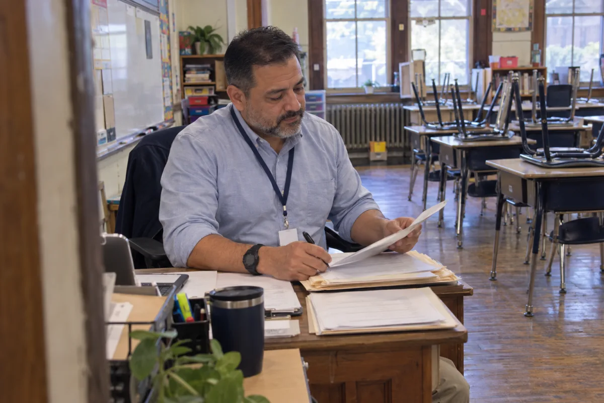The teacher counts the permission slips: twenty-one back, three still to chase